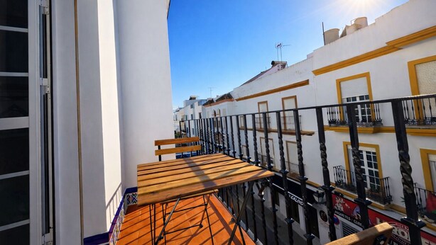 A balcony with a wooden bench, white buildings with yellow trim, and a clear blue sky. - Apartamento Arrumbadores con terraza en Conil (conil de la frontera)