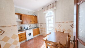 A kitchen with wooden cabinets, a washing machine, a microwave, and a dining table with chairs. - Apartamento Arrumbadores con terraza en Conil (conil de la frontera)