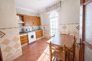 A kitchen with wooden cabinets, a washing machine, a microwave, and a dining table with chairs. - Apartamento Arrumbadores con terraza en Conil (conil de la frontera)