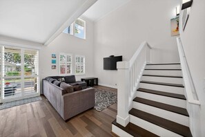 A spacious living room with a grey sofa, a staircase, and a view of the outdoors.