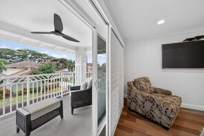 A balcony with a ceiling fan, a cushioned bench, a patterned sofa, and a TV mounted on the wall.