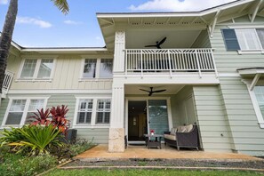 A two-story house with a balcony, a patio with outdoor furniture, and a large window.