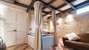 Une pièce avec un mur en pierre, une porte blanche, une table de massage, un canapé marron et des carreaux de sol à motifs.