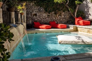 A swimming pool with a stone wall, red cushions, and a waterfall feature. - Palazzo Mandurino (Zollino)