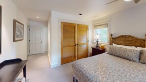 Un dormitorio con cama, mesita de noche, lámpara, armario de madera y puerta que da a otra habitación.