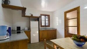 A kitchen with wooden cabinets, a refrigerator, a microwave, a sink, and a dining table with a fruit bowl. - Holiday Home "Camp Redo" with Mountain View, Pool, Garden, Terrace & Wi-Fi (Illes Balears)