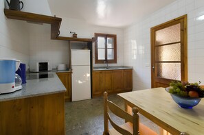 Eine Küche mit Holzausstattung, einem Kühlschrank, einer Mikrowelle, einem Spülbecken und einem Esstisch mit Obstschale.
