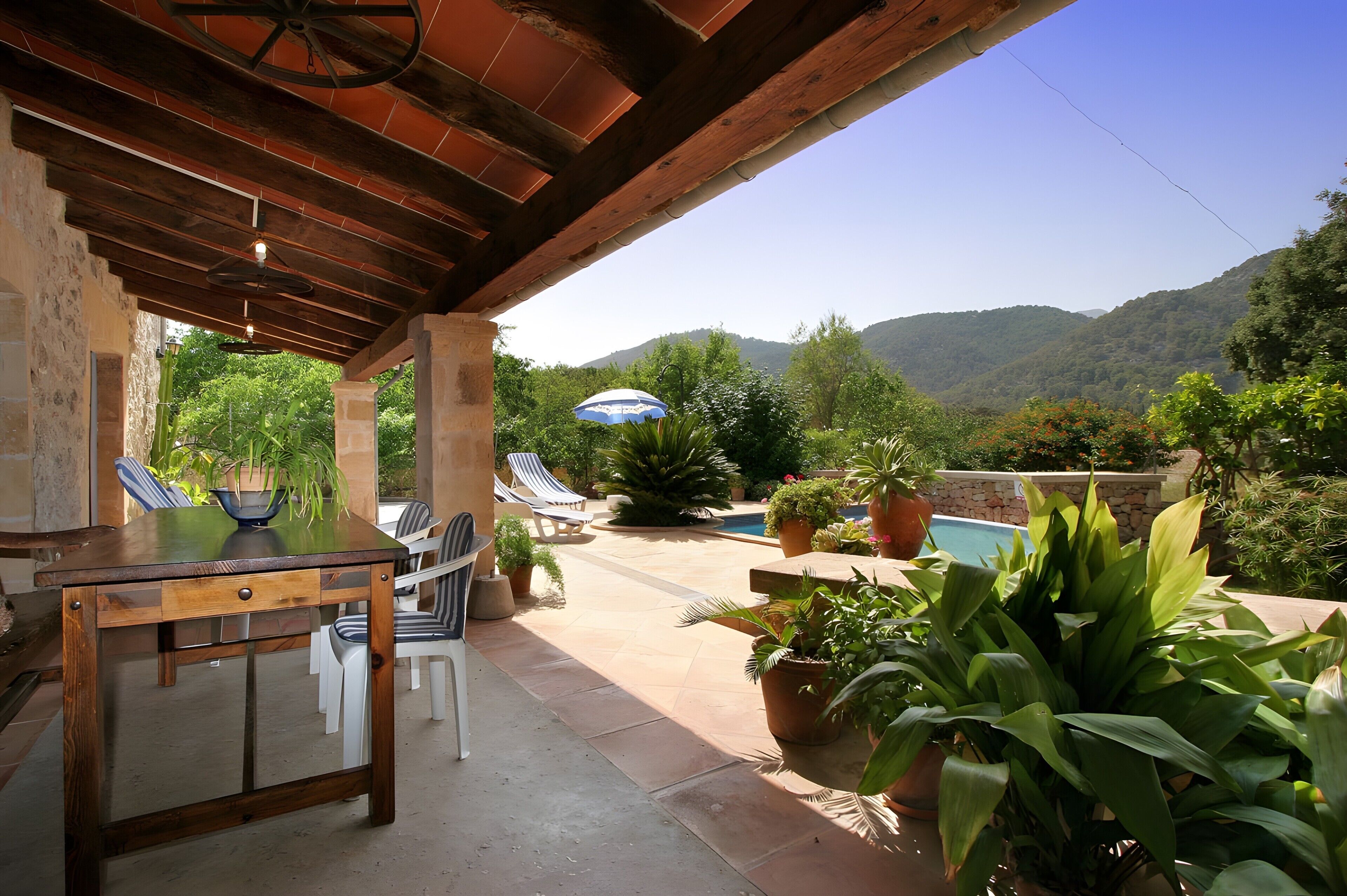 An outdoor patio with a table and chairs, a pool, and potted plants.