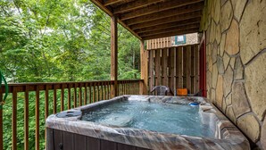 A hot tub on a wooden deck with a stone wall backdrop and a wooden railing. - Residing In The Highlands (GATLINBURG)