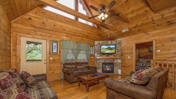 A log cabin interior with a fireplace, wooden furniture, and a ceiling fan. - Residing In The Highlands (GATLINBURG)