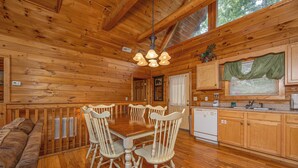 A wooden cabin interior with a dining table, chairs, a kitchen area, and a built-in bench. - Residing In The Highlands (GATLINBURG)