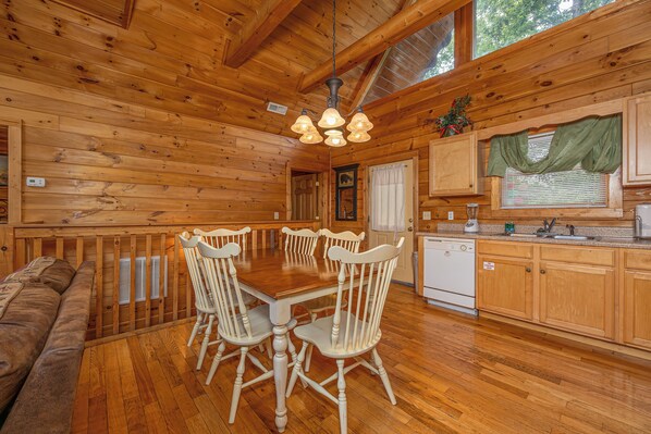 A wooden cabin interior with a dining table, chairs, a kitchen area, and a built-in bench. - Residing In The Highlands (GATLINBURG)