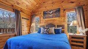 Camera da letto in una baita di legno, con un letto grande, due comodini e un'anta finestrata con tende.