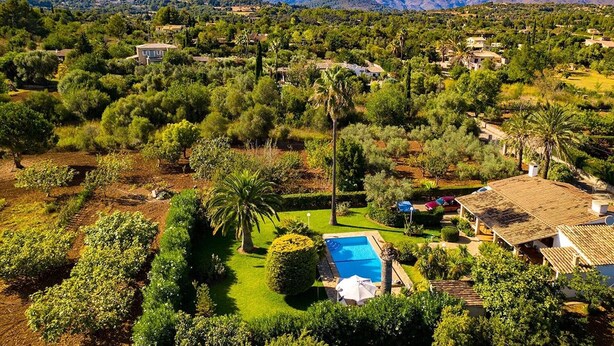 A residential area with a swimming pool, lush greenery, and houses with tiled roofs.