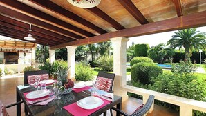 An outdoor patio with a dining table set for four, surrounded by greenery and a pool view.