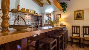 A kitchen with a wooden bar, bar stools, a sink, and a window with curtains.