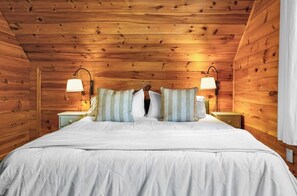 Ein schlicht eingerichtetes Schlafzimmer im Chalet-Stil mit einem Bett, zwei Nachttischlampen und gestreiften Kissen.