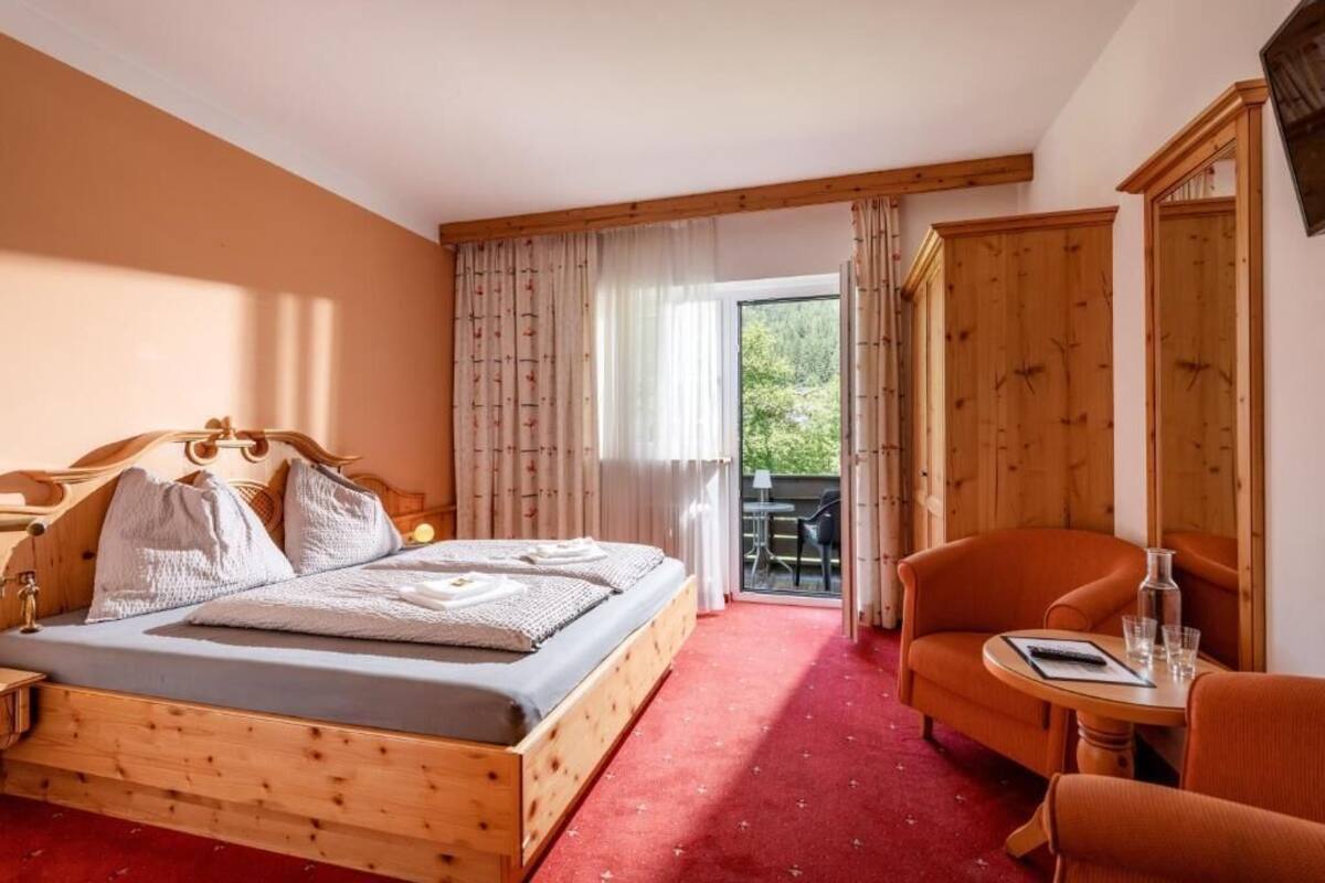 Ein Schlafzimmer mit einem hölzernen Bett, einem kleinen Tisch mit Stühlen, einem Kleiderschrank und einer Schiebeglastür zu einem Außenbereich.