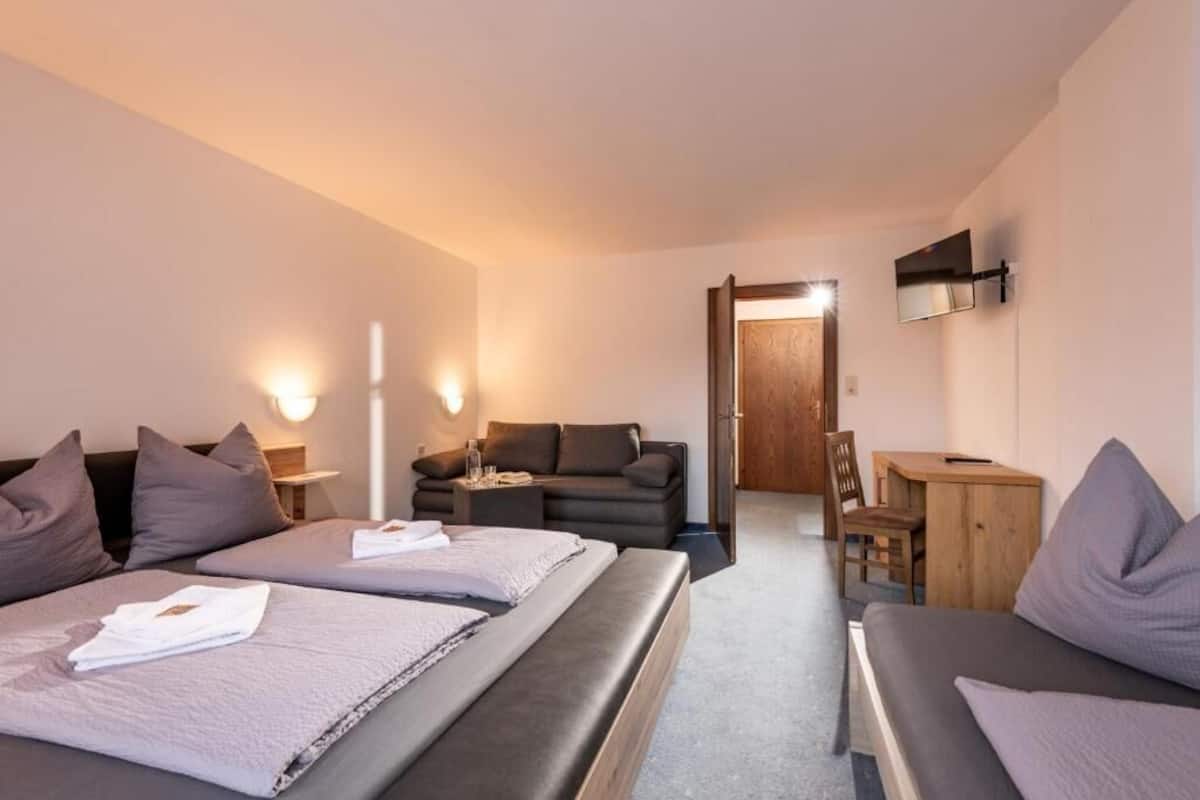 Ein Hotelzimmer mit zwei Betten, einer Couch, einem Schreibtisch und einem Fernseher.
