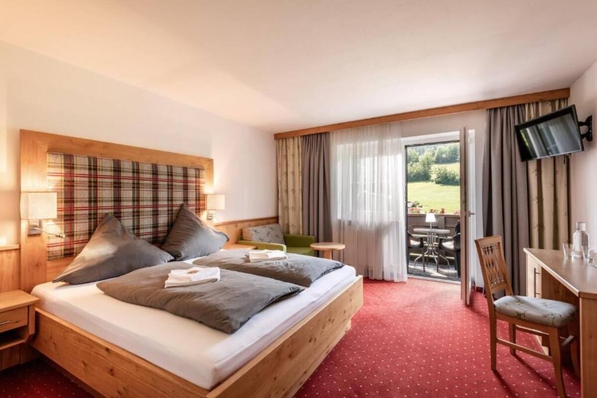 Ein Hotelzimmer mit Bett, Schreibtisch, Fernseher und Blick ins Freie.