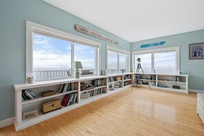 A room with large windows, a bookshelf, and a tripod. - Wharfside Watch – NEW Oceanfront Home! (Blue Hill)