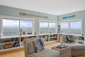 A coastal room with large windows, a bookshelf, two striped sofas, and a telescope. - Wharfside Watch – NEW Oceanfront Home! (Blue Hill)