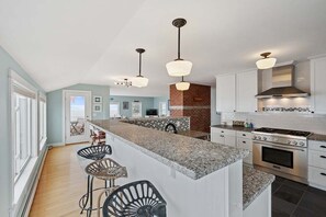A kitchen with a granite countertop, stainless steel appliances, and pendant lighting. - Wharfside Watch – NEW Oceanfront Home! (Blue Hill)