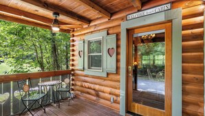 Eine Holzhütte mit einer Veranda, zwei Stühlen, einem Deckenventilator und einer Tür mit dem Schild 'Welcome to our Cabin'.