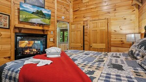 Ein holzgetäfeltes Zimmer im Chalet-Stil mit Kamin, einem Bett mit roter Decke und einer Steude.