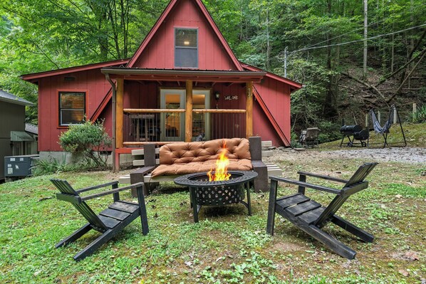 Une cabane rouge avec un foyer, deux fauteuils et un banc devant.