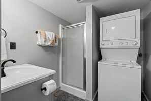 Une salle de bain avec un lavabo blanc, du papier toilette, un porte-serviettes avec une serviette, ainsi qu’un lave-linge et un sèche-linge intégrés.
