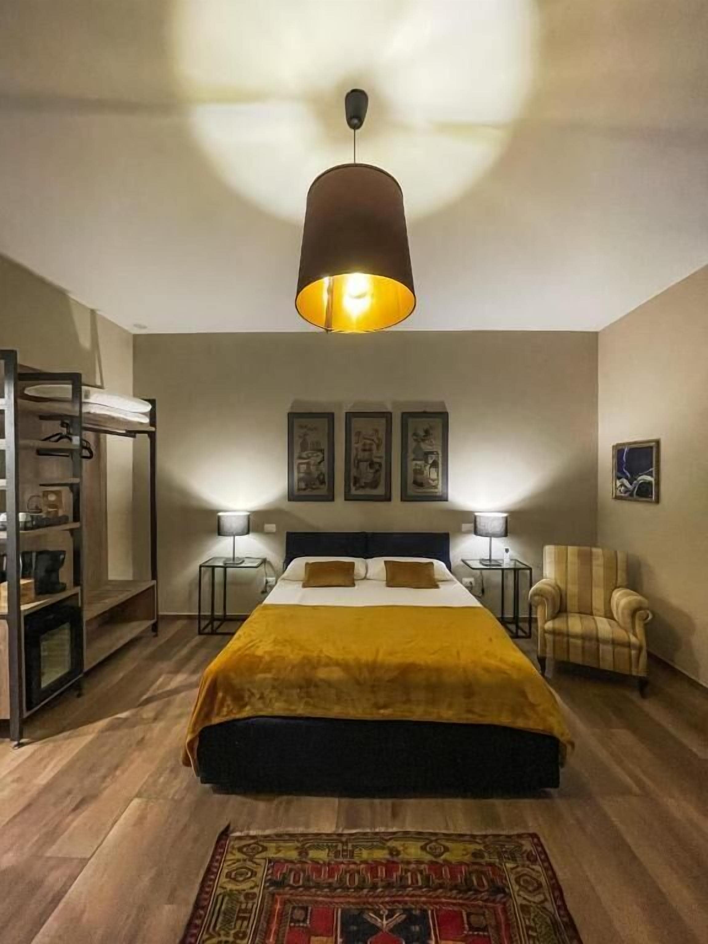 Ein Schlafzimmer mit Bett, Nachttischlampen, einem Sessel, einem Kleiderschrank und einer Pendelleuchte.