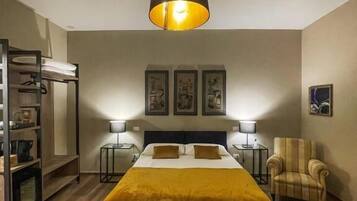 Ein Schlafzimmer mit Bett, Nachttischlampen, einem Sessel, einem Kleiderschrank und einer Pendelleuchte.
