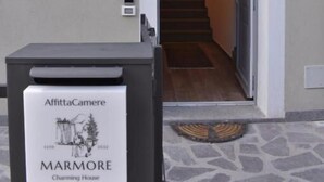 Fachada de un edificio con suelo de piedra, un letrero que dice 'AffittaCamere Marmore Charming House' y una escalera que da acceso al interior.
