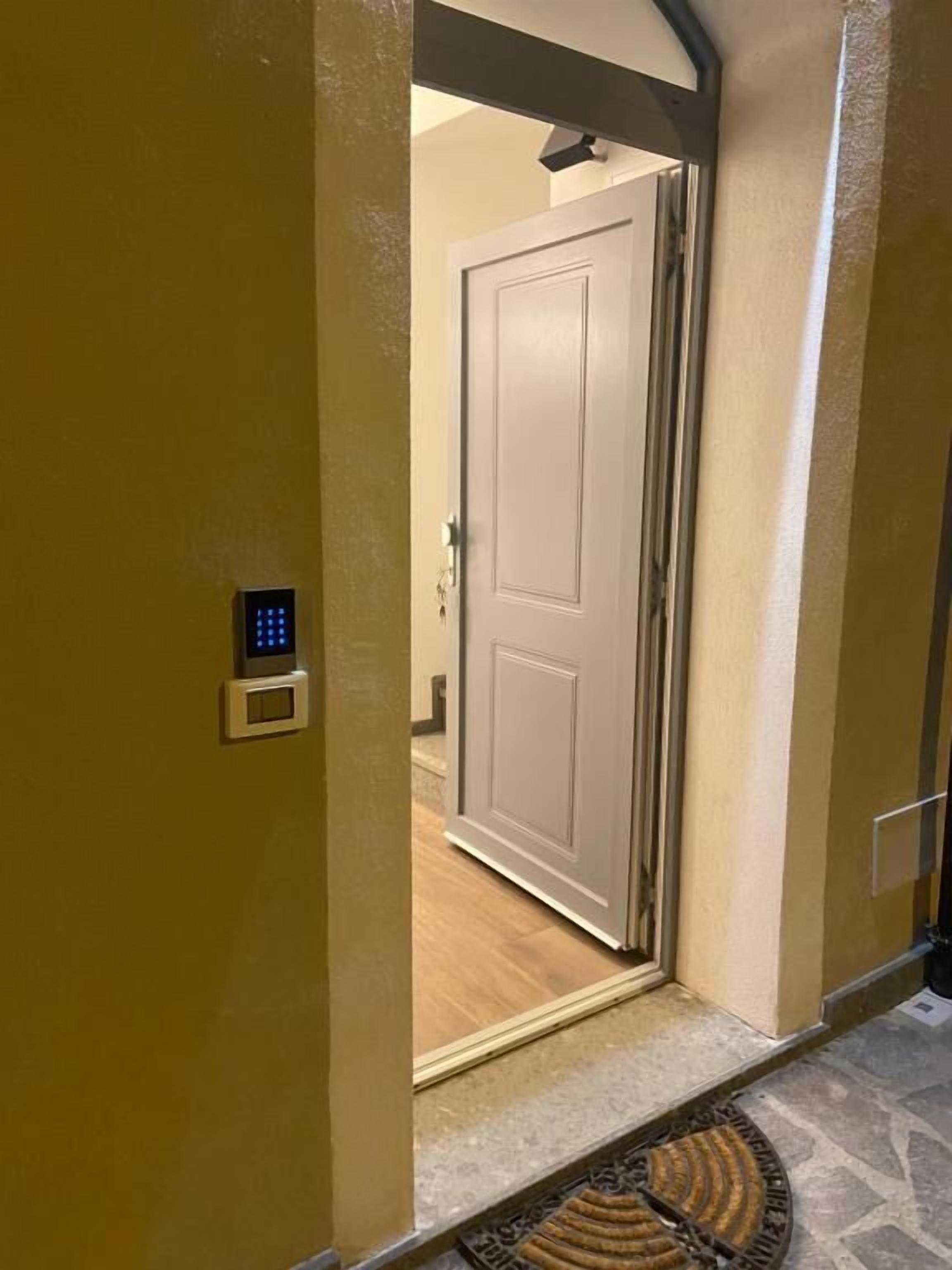 Un pasillo con una puerta, un panel de control en la pared y un felpudo estampado en el suelo.
