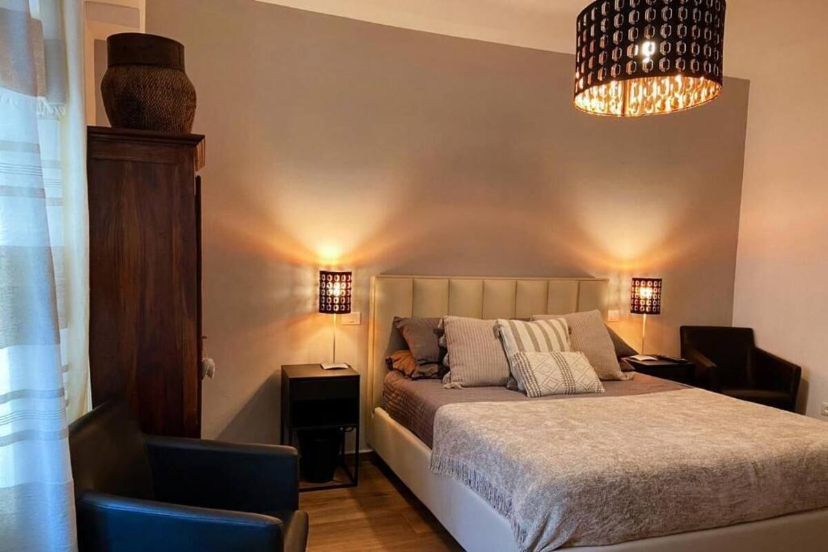 A bedroom with a bed, two bedside tables, a nightstand, a chair, and a hanging light fixture.