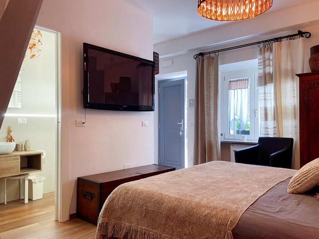 A bedroom with a bed, a TV mounted on the wall, a desk, a chair, and a window with curtains.