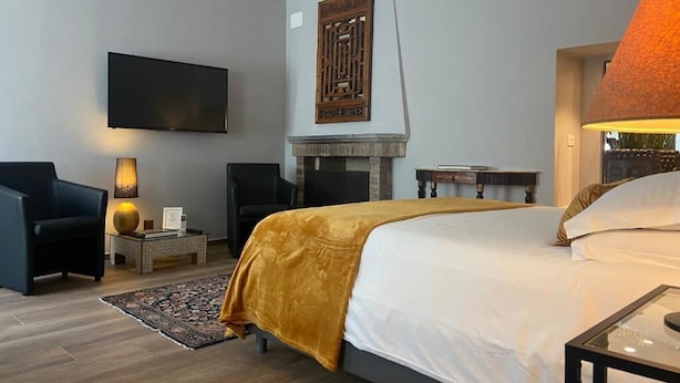 Una habitación de hotel moderna con una cama grande, televisor de pantalla plana, chimenea y un área de descanso con una lámpara.