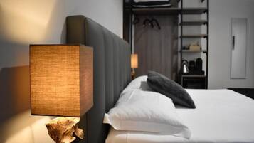 A hotel room with a bed, a nightstand with a lamp, and a wardrobe in the background.