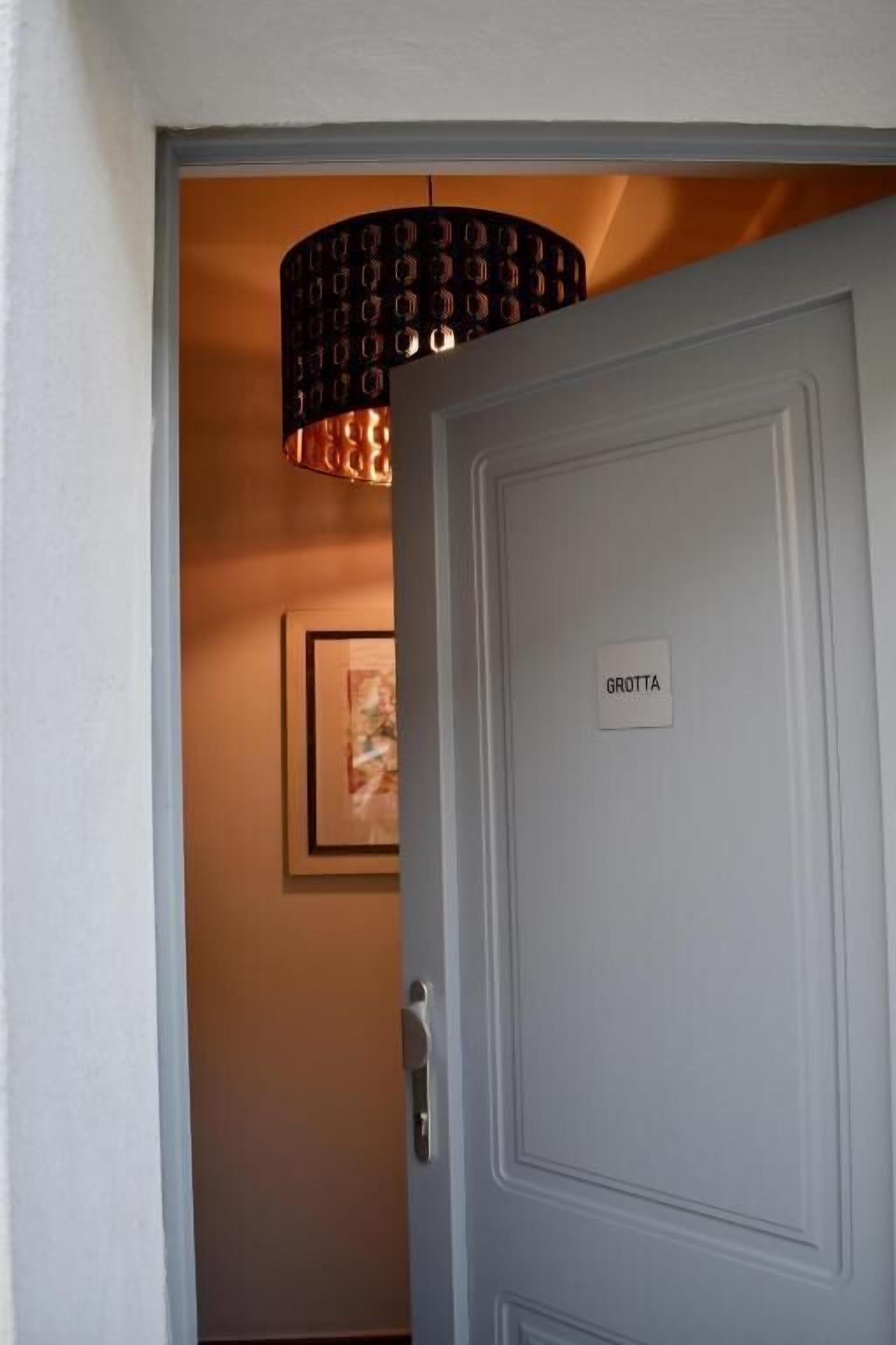 Una porta chiusa con un cartello che riporta la scritta 'GROTTA' e un lampadario decorativo sopra.