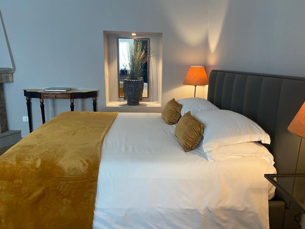 A hotel room with a bed, two lamps, a window with a view, and a small table with a book.