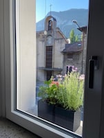 Vista desde una ventana de un edificio con una torre de campanas, una puerta y plantas en macetas.