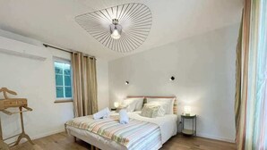 Een slaapkamer met een bed, nachtlampjes, een houten vloer, een raam met gordijnen en een plafondlamp.
