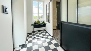 Een gang met een zwart-wit geruite vloer, een raam met uitzicht en een deur naar een andere kamer.