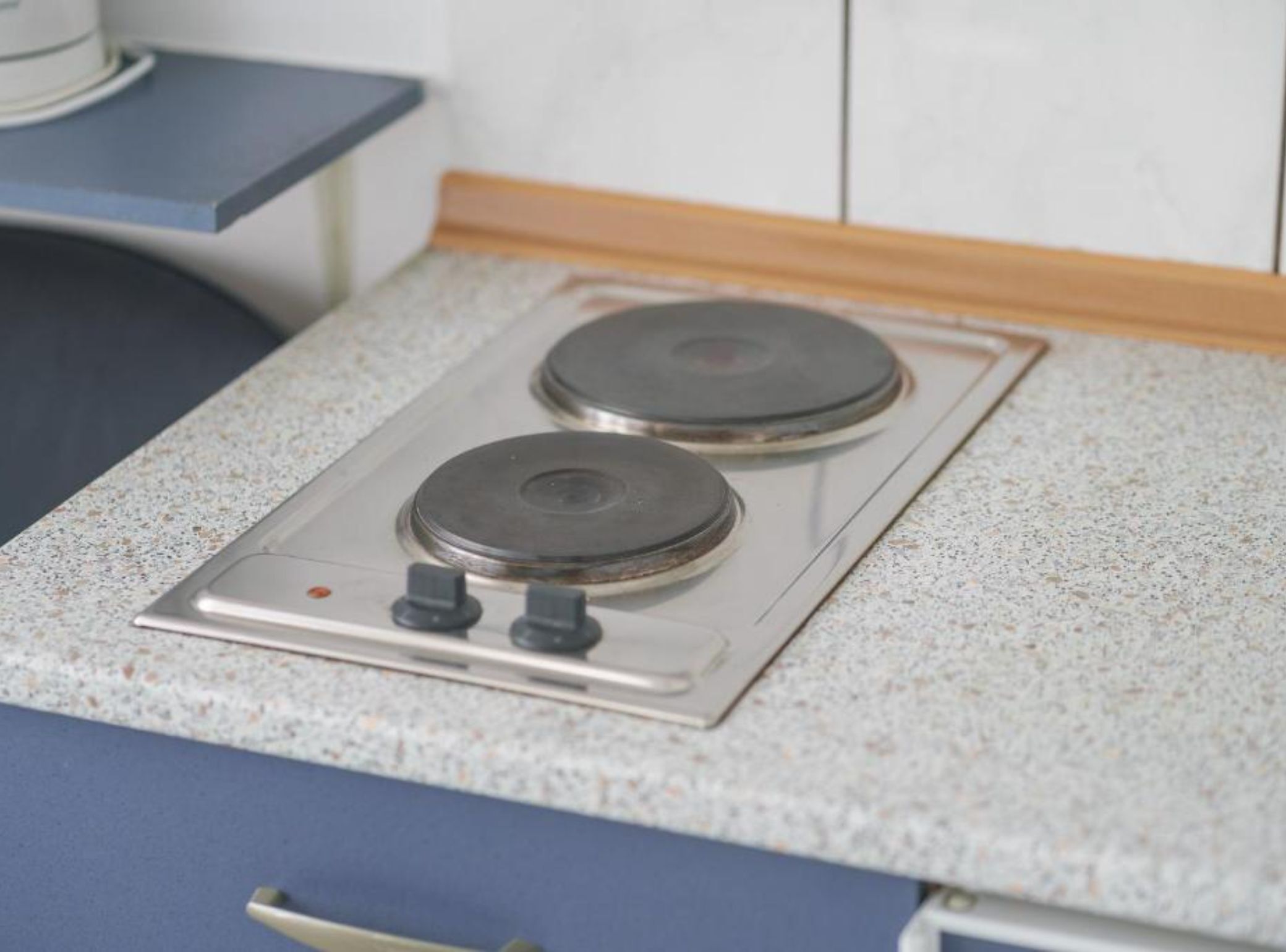 Une cuisine dotée de deux plaques de cuisson, d’un plan de travail bleu et d’un crédence blanc.