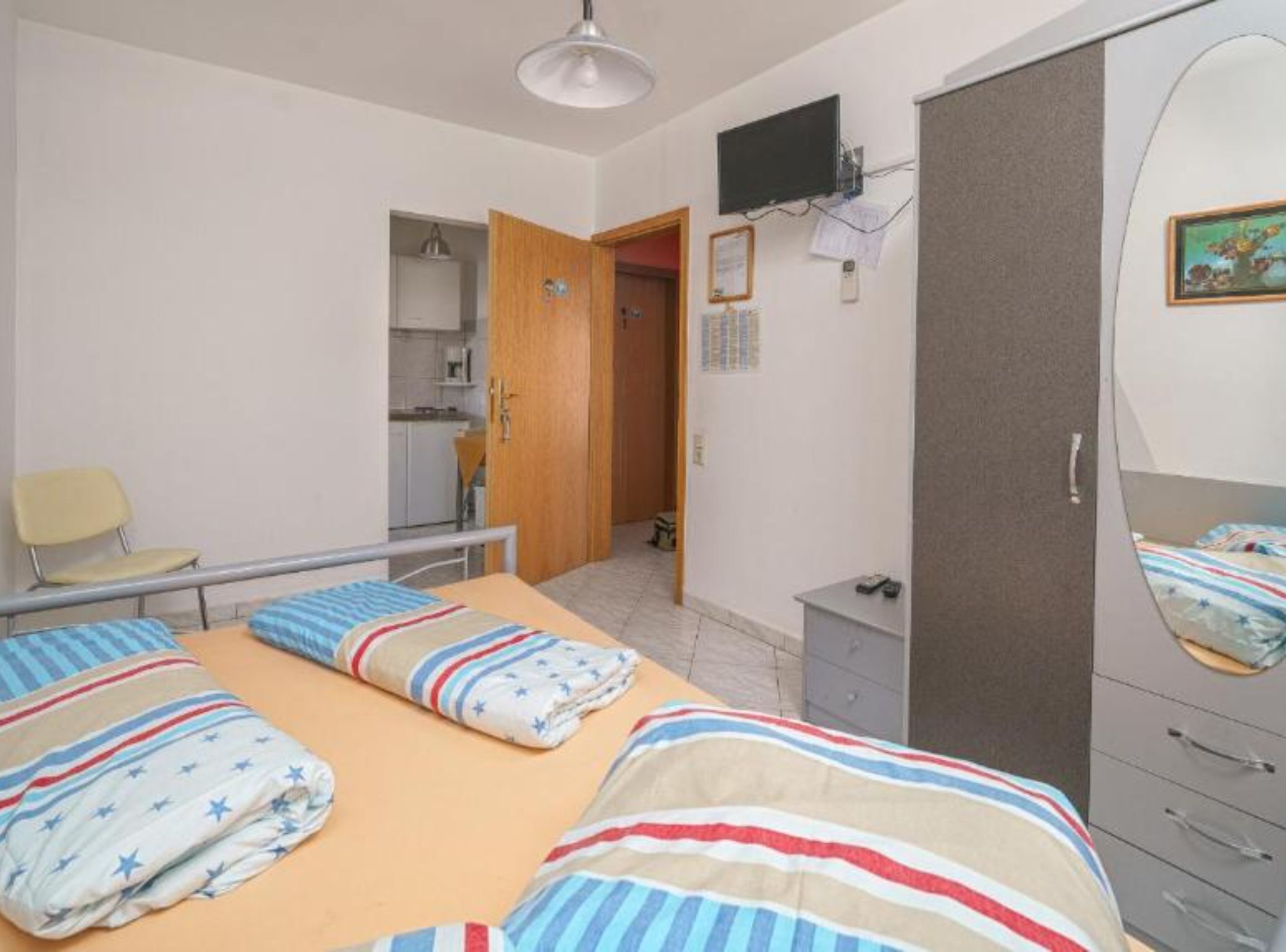 Ein Schlafzimmer mit einem Bett, einem Sessel, einem Kleiderschrank, einem Fernseher und einem Schreibtisch.