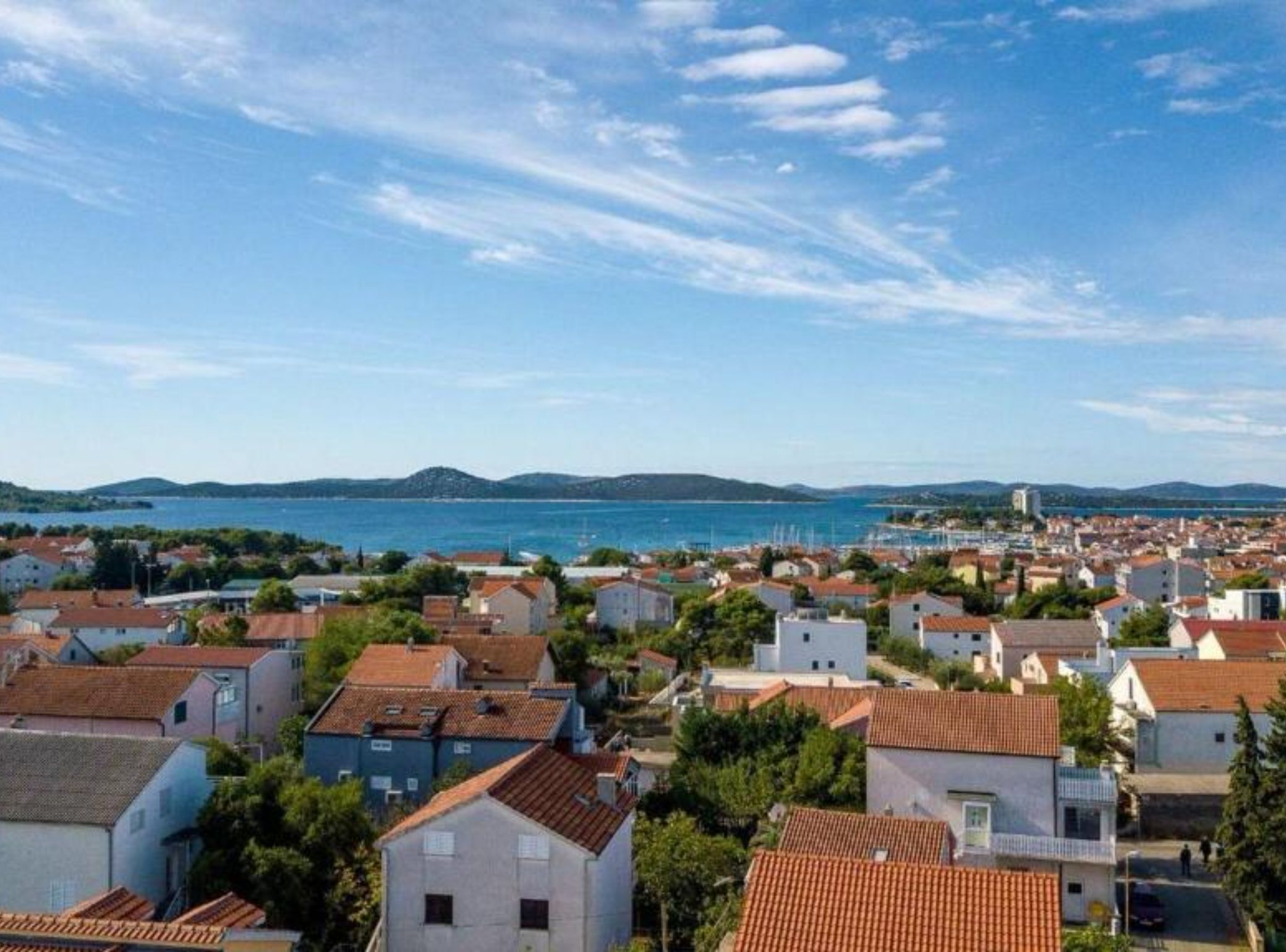 Un paese costiero con edifici dai tetti in terracotta, un cielo azzurro limpido e vista sul mare.