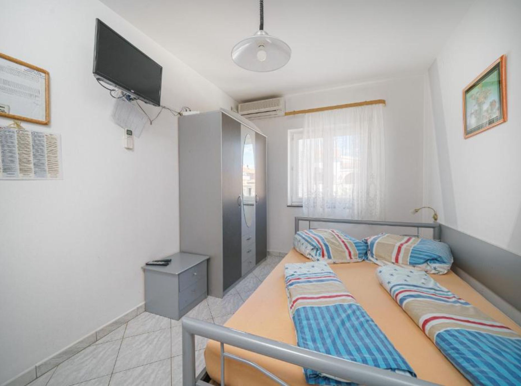 Un dormitorio con cama, escritorio, armario, televisor y ventana con cortinas.