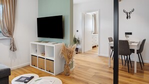 A modern living room with a flat-screen TV, a dining area with a table and chairs, and a decorative wall with a deer head.