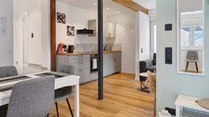 A modern kitchen with white cabinets, a wooden ceiling beam, and a dining area with grey chairs and a white table.